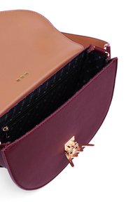 Burgunderfarbene Handtasche mit glatter Oberfläche und einem goldfarbenen Metallverschluss. Das Innere hat ein schwarzes Futter mit Punkten und eine Reißverschlusstasche.