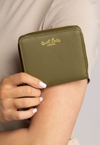 Alyvuogių spalvos odinė piniginė su struktūriniu paviršiumi, auksine išspausta prekės ženklo logo, užtrauktuku uždaroma ir kompaktiška stačiakampio formos.
