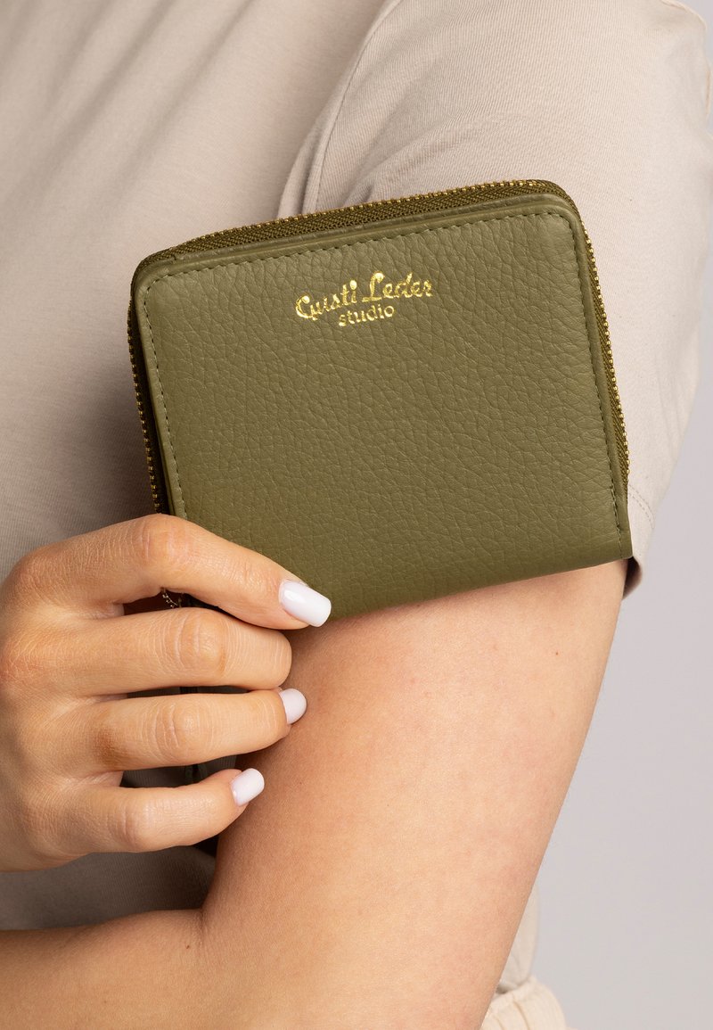 Alyvuogių spalvos odinė piniginė su struktūriniu paviršiumi, auksine išspausta prekės ženklo logo, užtrauktuku uždaroma ir kompaktiška stačiakampio formos.