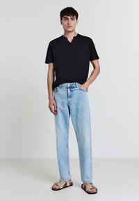 Maglietta henley nera a maniche corte, jeans azzurri a vita alta e comodi, e sandali beige. Look casual con una finitura testurizzata.