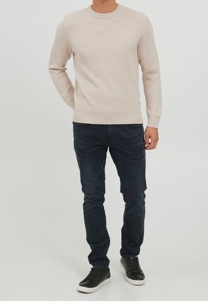 Hellbeiger strukturierten Pullover mit Rundhalsausschnitt, kombiniert mit dunkelblauen, enganliegenden Jeans und schwarzen Turnschuhen. Gerippte Bündchen und Saum.