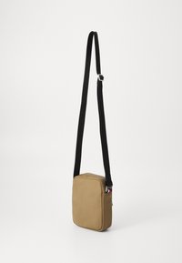 Geantă crossbody de culoare bej, cu o textură netedă, formă rectangulară, curea ajustabilă neagră și accesorii din argint. Închidere cu fermoar în partea de sus, cu detaliu logo.