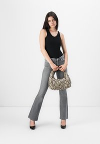 Svart ermeløs body, grå flared jeans, og en beige veske med ormeskinnmønster. Modellen har på seg svarte lakksko. Minimalistisk bakgrunn.