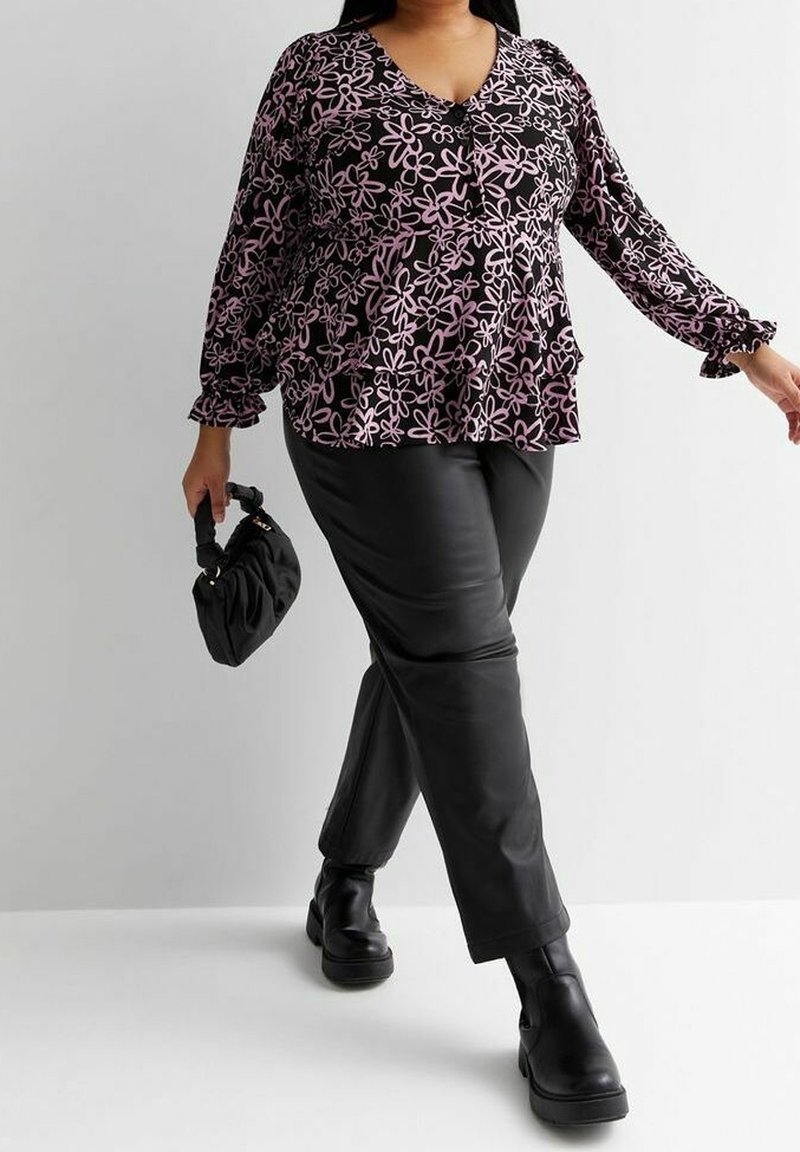 Femme marchant, portant un pantalon en cuir synthétique noir, des bottes noires, un chemisier à manches longues violet à fleurs, et portant un petit sac à main noir.