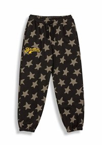 Zwarte joggingsbroek met groot beige sterpatroon, elastische tailleband, trekkoord en geborduurde gele tekst "grimy" op de linkerpijp.
