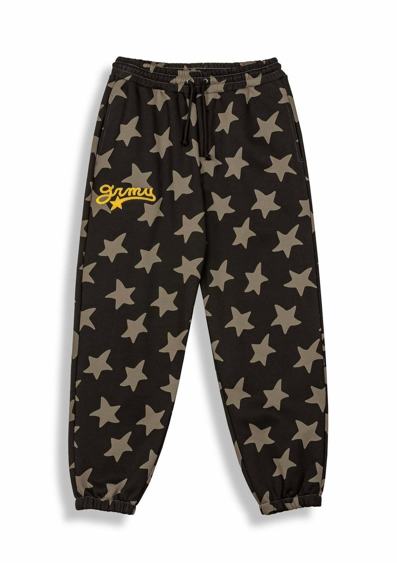 Pantalones de chándal negros con un gran patrón de estrellas beige, cinturilla elástica, cordón y el texto bordado "grimy" en amarillo en la parte frontal de la pierna izquierda.