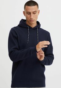 Marineblauwe hoodie van zachte stof, met een trekkoord capuchon, ribbels aan de mouwen en een relaxte pasvorm. Gladde textuur met minimale details.