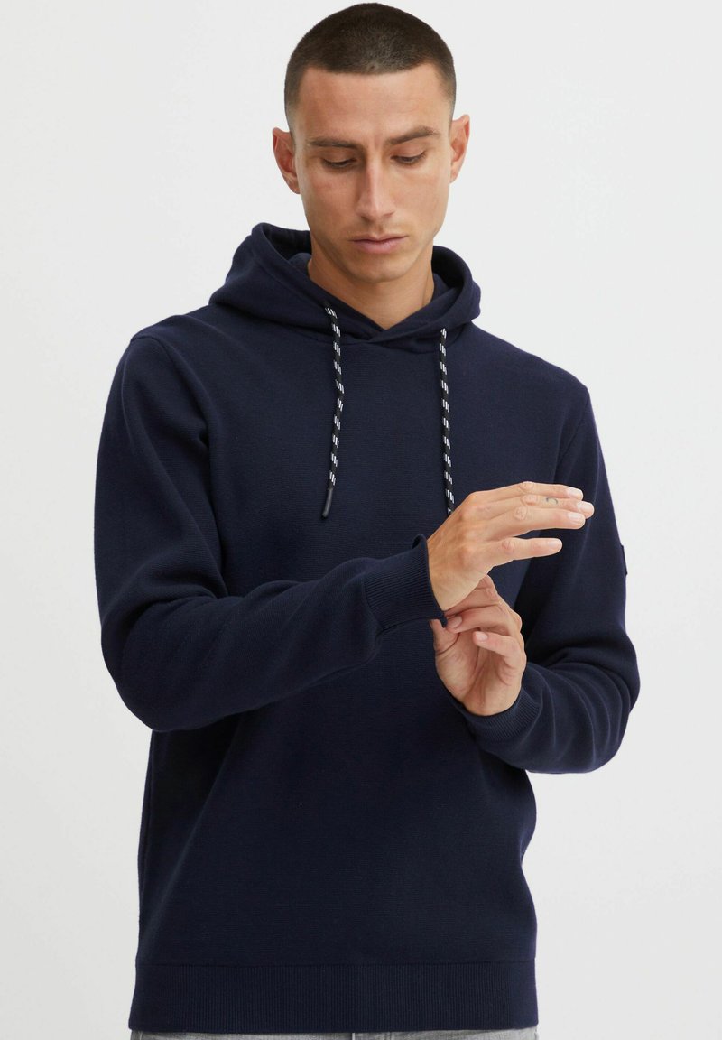 Marineblauwe hoodie van zachte stof, met een trekkoord capuchon, ribbels aan de mouwen en een relaxte pasvorm. Gladde textuur met minimale details.