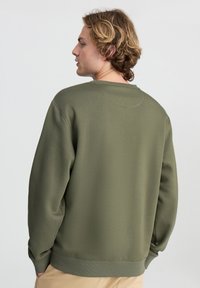 Felpa verde olivo con vestibilità comoda, polsini e orlo a coste, tessuto dalla texture liscia e scollatura rotonda. Design semplice senza grafiche.