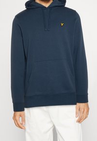 Felpa con cappuccio blu navy, dotata di tasca a marsupio, polsini a costine e logo giallo ricamato sul petto. Realizzata in un tessuto morbido con una texture liscia.