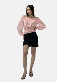 Lyserød off-the-shoulder bluse med smocket talje, parret med en sort indbundet mini-nederdel. Model i stribede sorte hæle. Neutral baggrund.