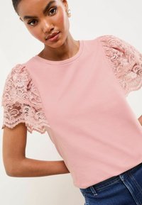Chemise rose avec des manches en dentelle bouffantes, fabriquée en tissu doux avec une texture lisse. Encolure ronde simple et design ajusté.