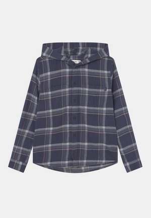 Camisa de franela con capucha de color azul marino con patrón de cuadros en gris y beige, botones al frente, mangas largas y un bolsillo en el pecho etiquetado con una pequeña etiqueta.