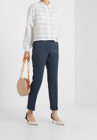 Wit gestreepte overhemd, marineblauwe patroon broek, crème hakken en een ronde beige tas met een meerkleurige schouderband.