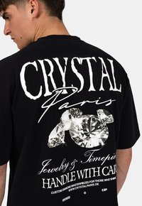Zwart T-shirt met korte mouwen, met grote witte tekst en diamantgrafieken op de achterkant. Het materiaal lijkt zacht en heeft een relaxte pasvorm.