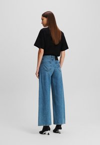 Weite, dunkelblaue Jeans aus Denim mit hoher Taille, dezentem Taschenstitching und entspanntem Schnitt. Kombiniert mit einem schwarzen T-Shirt.