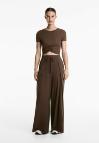 Top corto marrone con arricciature laterali, abbinato a pantaloni larghi marroni con vita regolabile. Tessuto morbido ed elastico.