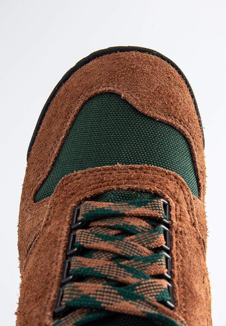 Chaussure en daim marron et en tissu texturé vert avec des accents noirs, dotée d'un design à lacets et d'une zone de orteil renforcée.