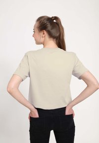 Lichtgrijze, kortop mouw t-shirt met een ronde hals, gemaakt van zachte stof, gezien van de achterkant, gedragen met zwarte jeans.
