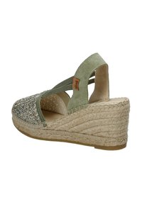 Sandalo con tacco a zeppa in suede verde, con tacco in juta intrecciata. Presenta una punta intrecciata, cinghie incrociate elastiche e un rivestimento interno liscio beige.