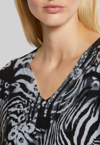 Strickpullover mit einem schwarz-grauen Zebra-Muster, V-Ausschnitt, geripptem Kragen und weicher Textur. Der Fokus liegt auf dem Oberkörperbereich.