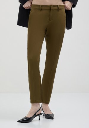 Pantaloni su misura verde oliva con una texture liscia, caratterizzati da un girovita medio, tasche laterali e un design slim fit. Abbinati a tacchi neri.