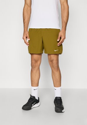 Alyvos žalios sportinės šortai su baltu Nike logotipu, derinami su juodais sportiniais batais ir baltais kojiniais, dėvimi su baltu marškinėliu.