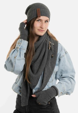 Grijze gebreide beanie, bijpassende sjaal met textuur en zijstrikken, en vingerloze handschoenen; gelaagd over een spijkerjack tegen een witte achtergrond.