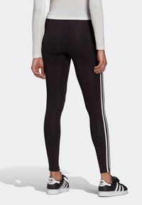 Black leggings with white side stripes, featuring a smooth texture and slim fit. Matched with black and white sneakers.