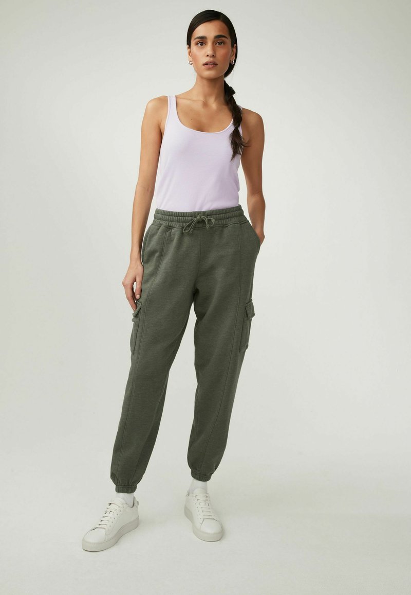 Top fără mâneci de culoare violet deschis, asociat cu pantaloni de trening cargo de culoare verde măsliniu, cu mansete elastice și buzunare laterale, purtați cu adidași albi.