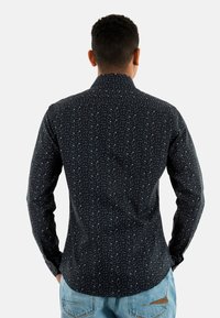 Chemise noire à manches longues ornée d'un motif de petits points bleu clair, col boutonné, et en tissu doux avec une coupe ajustée.