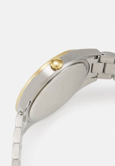 Silver and gold-tone wristwatch with a round case, metallic band, and a crown on the side. Smooth finish with a minimalist design.