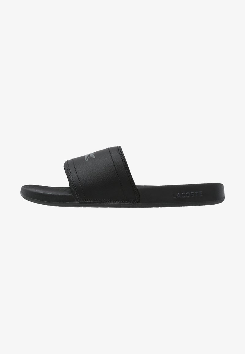 Sandales slide noires avec une bride texturée et une semelle intérieure lisse, présentant un logo Lacoste discret. Design profilé avec des accents minimalistes.