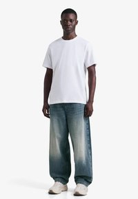 Vit bomulls-t-shirt kombinerad med lösa, ljusblå urtvättade jeans. Outfiten kompletteras med beigea sneakers. Enkel och avslappnad stil.