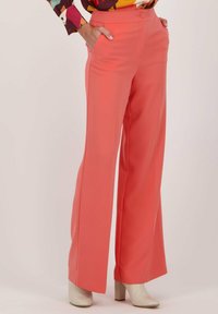 Koraal kleurige wijde broek van soepele stof, met zijzakken en een knoopsluiting, gecombineerd met lichtgekleurde hakken.