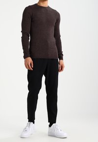 Pull à manches longues marron côtelé associé à un pantalon de jogging noir et des baskets blanches. Le tissu est texturé avec une coupe ajustée.