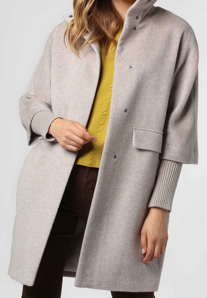 Cappotto in misto lana grigio chiaro con colletto alto, chiusure a scatto e tasche laterali. Presenta polsini a coste e una vestibilità rilassata.