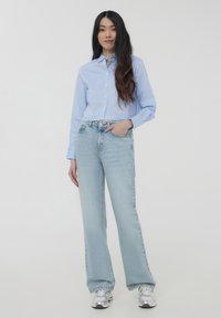 Camicetta a righe blu e bianche con bottoni, jeans a gamba larga blu chiaro e sneaker argento, caratterizzati da una vestibilità rilassata e un design classico.