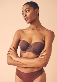 Soutien-gorge marron sans bretelles avec bonnets moulés et armatures, assorti à un slip bikini taille basse. Tissu lisse et design sans coutures.