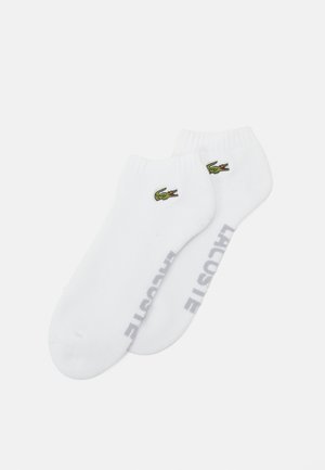 Chaussettes blanches mi-mollet en mélange de coton, présentant un logo crocodile brodé vert et le texte "LACOSTE" en gris sur le côté.