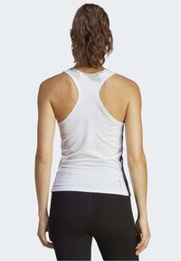 Canotta sportiva bianca con design a rovesci, caratterizzata da una texture liscia e dettagli neri ai lati. La vista posteriore mostra una silhouette aderente e il logo.
