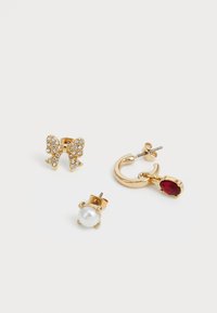Tres pendientes de oro: un lazo con cristales transparentes, un arete de perla y un aro con un encantador colgante de gema roja.