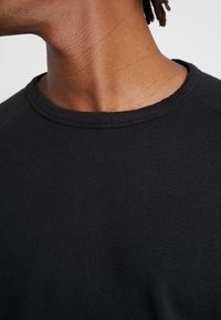 Schwarzes T-Shirt mit kurzen Ärmeln, ausgestattet mit einem Rundhalsausschnitt und strukturiertem Strickmaterial, aus der Perspektive von Hals und Schulter abgebildet.