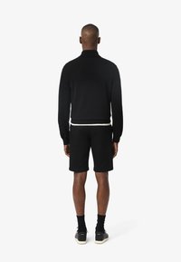 Pull-over noir en tricot avec un col, associé à un short noir. Design à coupe régulière, texture lisse et rehaussé d'une ceinture contrastante.
