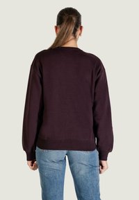 Ciemnofioletowa, luźna bluza z prążkowanymi mankietami i paskiem na dole, zestawiona z jasnoniebieskimi dżinsami, widziana od tyłu.