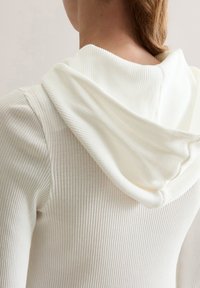 Witte geribde hoodie met een zachte textuur. Heeft een ruime capuchon en een getailleerd ontwerp, met een subtiel verticaal streepjespatroon.