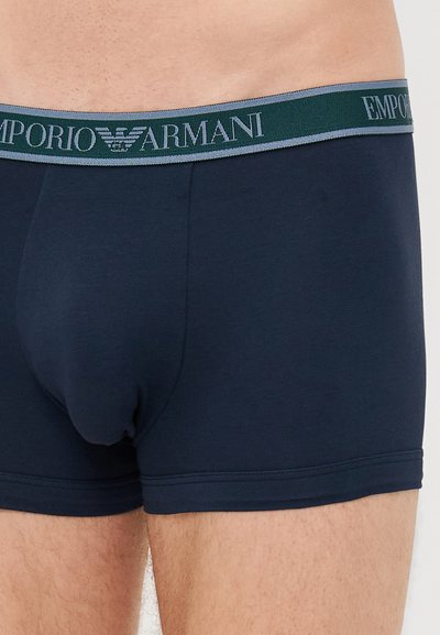 Marineblaue Baumwoll-Boxershorts mit einem breiten, elastischen Bund, der das Logo "Emporio Armani" in kontrastierenden Farben zeigt. Glatte Textur.