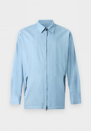 Veste bleu clair à manches longues avec fermeture éclair à l'avant, deux poches latérales zippées et un col classique sur fond uni.