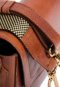 Borsa in pelle marrone con superficie texture, caratterizzata da tessuto a scacchi nero e beige in contrasto, hardware dorato e dettagli di cucitura visibili.