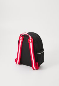 Rucsac negru cu bretele cu dungi roșii și albe, formă rotunjită, textură netedă, dotat cu un buzunar frontal și fermoare. Design minimalist.
